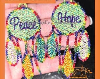 Peut inclure: Deux boucles d'oreilles en forme d'attrape-rêves colorées avec des plumes. Le cercle supérieur de chaque boucle d'oreille est brodé avec les mots "Peace" et "Hope".
