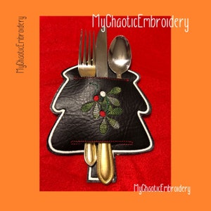 May include: A black felt Christmas tree-shaped cutlery holder with a green and red embroidered holly design. The holder has a pocket for a fork, knife, and spoon.