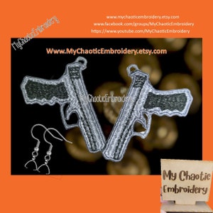 May include: Two silver embroidered gun earrings with black accents. The earrings are hanging from silver hooks. The earrings are on a brown background with the text "My Chaotic Embroidery" in white.