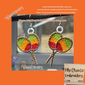 Puede incluir: Un par de pendientes con un par de maracas con bordado rojo, amarillo y verde. Los pendientes son de plata y tienen un bucle blanco en la parte superior. Los pendientes están sobre un fondo blanco. El texto "My Chaotic Embroidery" es visible en la imagen.