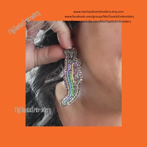 May include: A handmade, iridescent beaded earring in the shape of a stylized figure. The earring features a mix of purple, green, blue, and yellow beads. The text "MyChaoticEmbroidery" is visible in the image.