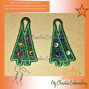 May include: Embroidered Christmas tree earrings with colorful gem accents. The green trees have a detailed outline and are adorned with red, yellow, and clear gems. The earrings are shown with silver earring hooks. The text "My Chaotic Embroidery" is also visible.