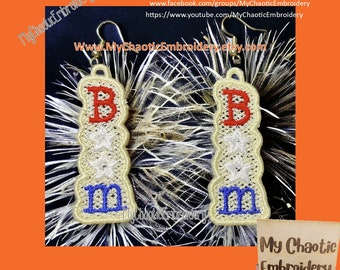 Può includere: Un paio di orecchini ricamati con le lettere "B" e "M" in rosso, bianco e blu. Gli orecchini sono appesi a ganci dorati e sono su uno sfondo marrone.