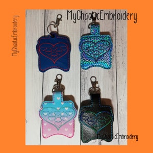 Puede incluir: Cuatro porta-gel hidroalcohólico diferentes con llaveros. Los porta-gel son de tela y tienen forma de corazón con un diseño bordado. Los colores son azul, verde azulado, rosa y negro.