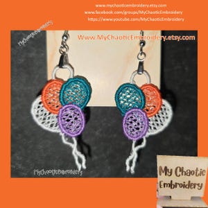 May include: A pair of handmade earrings featuring a cluster of colorful, embroidered balloons. The balloons are in shades of teal, orange, purple, and white. The earrings are attached to silver hooks.
