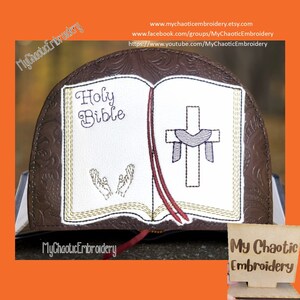 May include: Embroidered design of a closed book with the words "Holy Bible" on the cover. The book is open to reveal a cross with a heart and a pair of hands in prayer. The design is stitched on a brown leather-like material.