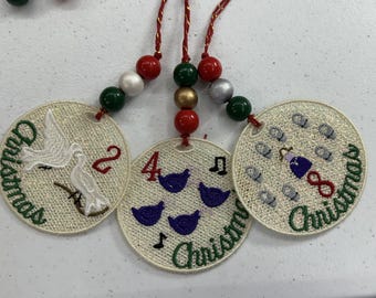 May include: Embroidered Christmas decorations with red, green, gold, and silver beads. Each circular ornament displays a different design: a dove, four birds, and eight bells. The word "Christmas" is embroidered in green on each.