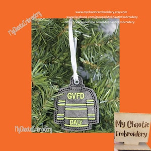 May include: A gray and yellow firefighter jacket ornament with the text "GVFD" and "DALY" embroidered on it. The ornament is hanging on a Christmas tree.