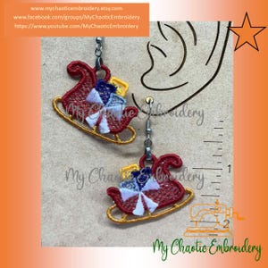 May include: Embroidered Christmas sleigh earrings. The earrings feature a red sleigh with yellow runners, and a colorful gift. The earrings are suspended from silver-colored hooks. The text "My Chaotic Embroidery" is visible.