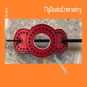 May include: Red fabric hair stick with a circle design and black stitching. The stick is black and has a hole in the center of the circle. The text "MyChaoticEmbroidery" is visible twice in the image.