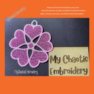 May include: A pink embroidered design of four hearts in a flower shape. The design is on a black background and has a small loop at the top. The text "My Chaotic Embroidery" is written on a brown background below the design.
