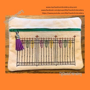 May include: A white zippered pouch with a purple tassel. The pouch features an embroidered design of a black wrought iron fence with colorful flowers growing on it. The text "MyChaoticEmbroidery" is written on the pouch.