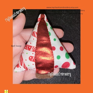 Può includere: Un ornamento per albero di Natale rosso, bianco e verde con un nastro rosso al centro. L'ornamento misura 4x4 pollici ed è realizzato con ritagli di tessuto. L'ornamento è tenuto in una mano.