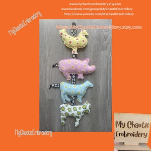 Puede incluir: Un conjunto de cinco juguetes de animales de tela colgados de una cuerda. Los juguetes son un pollo, un cerdo, una vaca y dos vacas. Los juguetes están hechos de una tela blanca con estampado de margaritas. Los juguetes están colgados en un fondo de madera. El texto "My Chaotic Embroidery" es visible en la imagen.