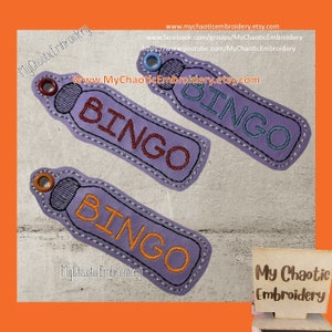 May include: Three purple fabric patches with the word "BINGO" embroidered in different colored thread. The patches are shaped like a bottle and have a small loop at the top. The text "My Chaotic Embroidery" is visible at the bottom of the image.