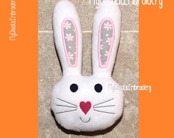 May include: White plush bunny head with pink ears and a red heart nose. The ears have a gray and white floral pattern. The bunny has black eyes and gray whiskers.