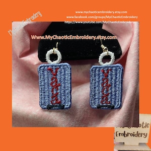 Puede incluir: Un par de pendientes bordados en azul y blanco con la palabra "Vacation" en hilo rojo. Los pendientes están colgados de un expositor negro.
