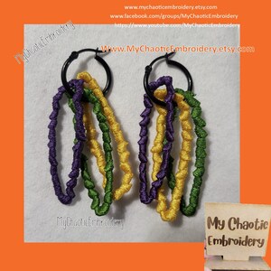 May include: A pair of black hoop earrings with dangling strands of purple, yellow, and green embroidery. The earrings are displayed against a white background with the text "My Chaotic Embroidery" and a website address.