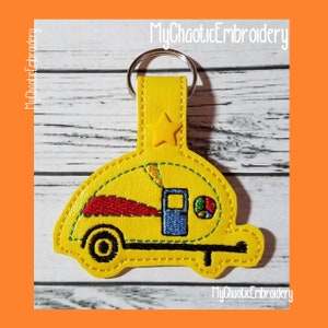 May include: Yellow embroidered camper van keychain with a star charm. The camper van has a blue door, red stripe, and a green and yellow circle on the side.  MyChaoticEmbroidery is written on the keychain.
