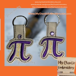 May include: Two purple and gold embroidered keychains with a rhinestone on top, shaped like the mathematical symbol pi. The keychains are on a light brown background with the text "My Chaotic Embroidery" on the bottom left and right.