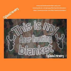 May include: Embroidered design on a camouflage fabric background. The design says "This is my deer hunting blanket" with two deer silhouettes on either side. The text is in a white thread with a black outline.
