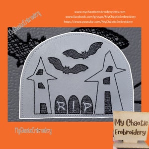 May include: Embroidered Halloween design featuring two gray houses with black windows, three black tombstones with the word "RIP" on them, and two black bats flying above the houses. The design is on a gray background.