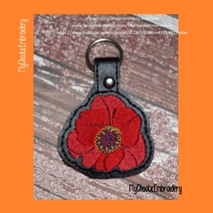 May include: A red poppy flower embroidered on a gray leather keychain. The keychain has a silver ring and a silver rivet. The text "MyChaoticEmbroidery" is printed on the bottom of the keychain.
