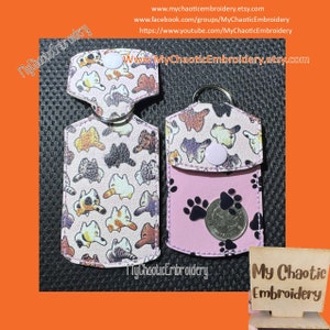 May include: Two pink keychains with a cat pattern and paw print designs. One keychain has a small pocket with a coin inside. The keychains are on a white background with the text "My Chaotic Embroidery" on the bottom.