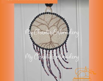 Peut inclure: Un attrape-rêves rond beige avec un motif d'arbre brun et des perles noires autour du bord. L'attrape-rêves a une frange de perles violettes et noires.