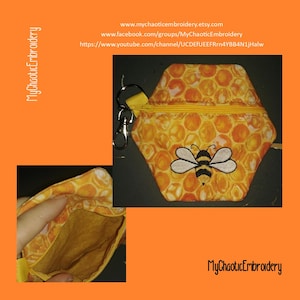 May include: A small hexagonal zippered pouch with a honeycomb pattern and a bee embroidery. The pouch has a yellow zipper and a silver key chain attached. The pouch is open to show the brown lining.