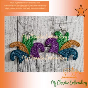 May include: A pair of Mardi Gras themed earrings with a purple, green, and gold design. The earrings are made of fabric and are attached to silver earring hooks.