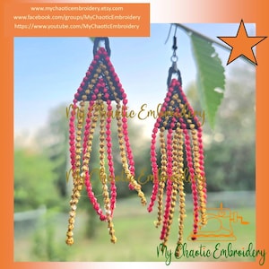 May include: Handmade macrame earrings with a triangular top in black, red, and gold, and dangling beaded fringe. The earrings are suspended from silver-tone hooks. The background is a blurred outdoor scene. Text on the image includes a website and social media links.