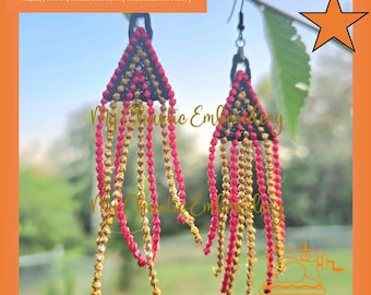 May include: Handmade macrame earrings with a triangular top in black, red, and gold, and dangling beaded fringe. The earrings are suspended from silver-tone hooks. The background is a blurred outdoor scene. Text on the image includes a website and social media links.