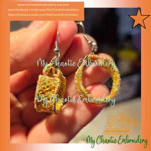 May include: A pair of gold and iridescent earrings with a circular and rectangular design. The earrings are made of embroidered fabric and have silver hooks.