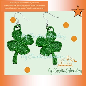 May include: A pair of green shamrock earrings with silver hooks. The shamrocks are made of a delicate lace-like material.