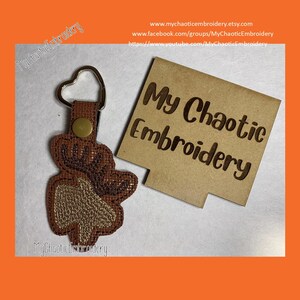 May include: A brown and gold embroidered moose keychain with a heart-shaped ring. The keychain is on a brown background with the text "My Chaotic Embroidery" in white.