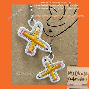 May include: A pair of earrings featuring a white embroidered design of two crossed yellow pencils with pink eraser details. The earrings are on a brown background with a ruler and the text "My Chaotic Embroidery".