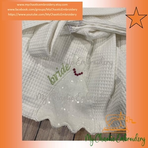 May include: White robe with a white sequined applique and the word "bride" embroidered in green thread. The applique has a red heart shape in the center.