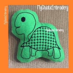 May include: Green felt turtle with black embroidered details. The turtle has a shell with a grid pattern and a small eye.