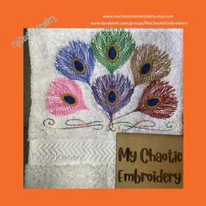 May include: A white towel with embroidered peacock feathers in pink, purple, green, brown, and red. The feathers are arranged in a fan shape. The towel has the text "My Chaotic Embroidery" printed on it.