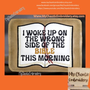 Puede incluir: Un parche de cuero marrón con bordado blanco que dice "Me desperté del lado equivocado de la Biblia esta mañana". El parche presenta una imagen estilizada de un libro cerrado con un marcador de cinta roja.