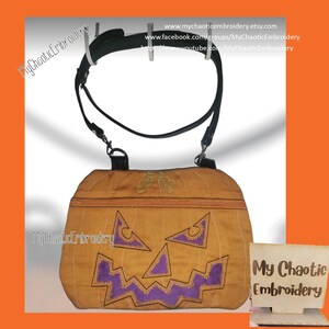May include: A brown pumpkin-shaped crossbody bag with a purple embroidered jack-o'-lantern face. The bag has a black adjustable strap and a zipper closure. The bag is labeled "My Chaotic Embroidery".