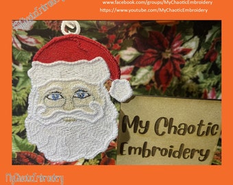 Pode incluir: Rosto de Papai Noel bordado em branco com um chapéu vermelho, uma barba branca e olhos azuis. A imagem está sobre um fundo marrom com o texto "My Chaotic Embroidery" em branco.