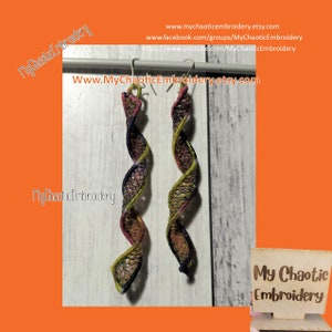 May include: A pair of long, colorful, spiral earrings with a black, pink, and yellow design. The earrings are hanging from a silver hook. The earrings are on a white wooden background. The text "My Chaotic Embroidery" is visible in the image.