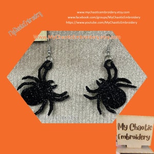 May include: A pair of black glitter spider earrings with silver-colored hooks. The earrings are shaped like spiders with eight legs and a rounded body. The image includes the text "My Chaotic Embroidery" and a website address.