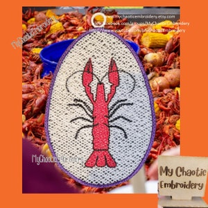 Puede incluir: Un parche bordado de forma ovalada blanca con un diseño de cangrejo rojo. El parche tiene un borde morado y está rodeado de una pila de cangrejos.