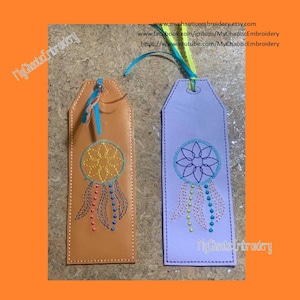 May include: Two leather bookmarks with a dreamcatcher design embroidered on them. The bookmarks are brown and purple and have a blue, yellow, and orange ribbon attached to the top. The text "My Chaotic Embroidery" is on the bottom of the purple bookmark.