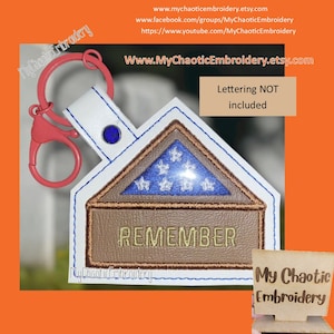 May include: A white leather keychain with a red swivel clasp and a blue gem. The keychain features a brown leather patch with the word "REMEMBER" embroidered in white. The patch is shaped like a folded American flag with blue stars on a white background. The text "Lettering NOT included" is visible in the upper right corner of the image.