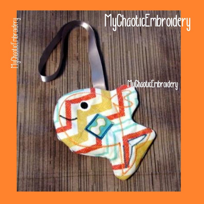 May include: A colourful fish-shaped fabric ornament with a loop for hanging. The fish is decorated with a yellow, orange and blue geometric pattern. The text "MyChaoticEmbroidery" is visible in the image.