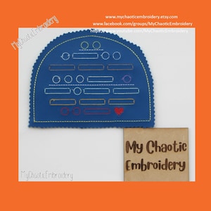 Può includere: Un'applicazione in feltro blu con un disegno di cerchi e rettangoli in vari colori, tra cui rosso, arancione, giallo, verde, blu e viola. L'applicazione ha la forma di un semicerchio e un bordo a festoni. Il testo "My Chaotic Embroidery" è stampato su un'etichetta di legno sotto l'applicazione.